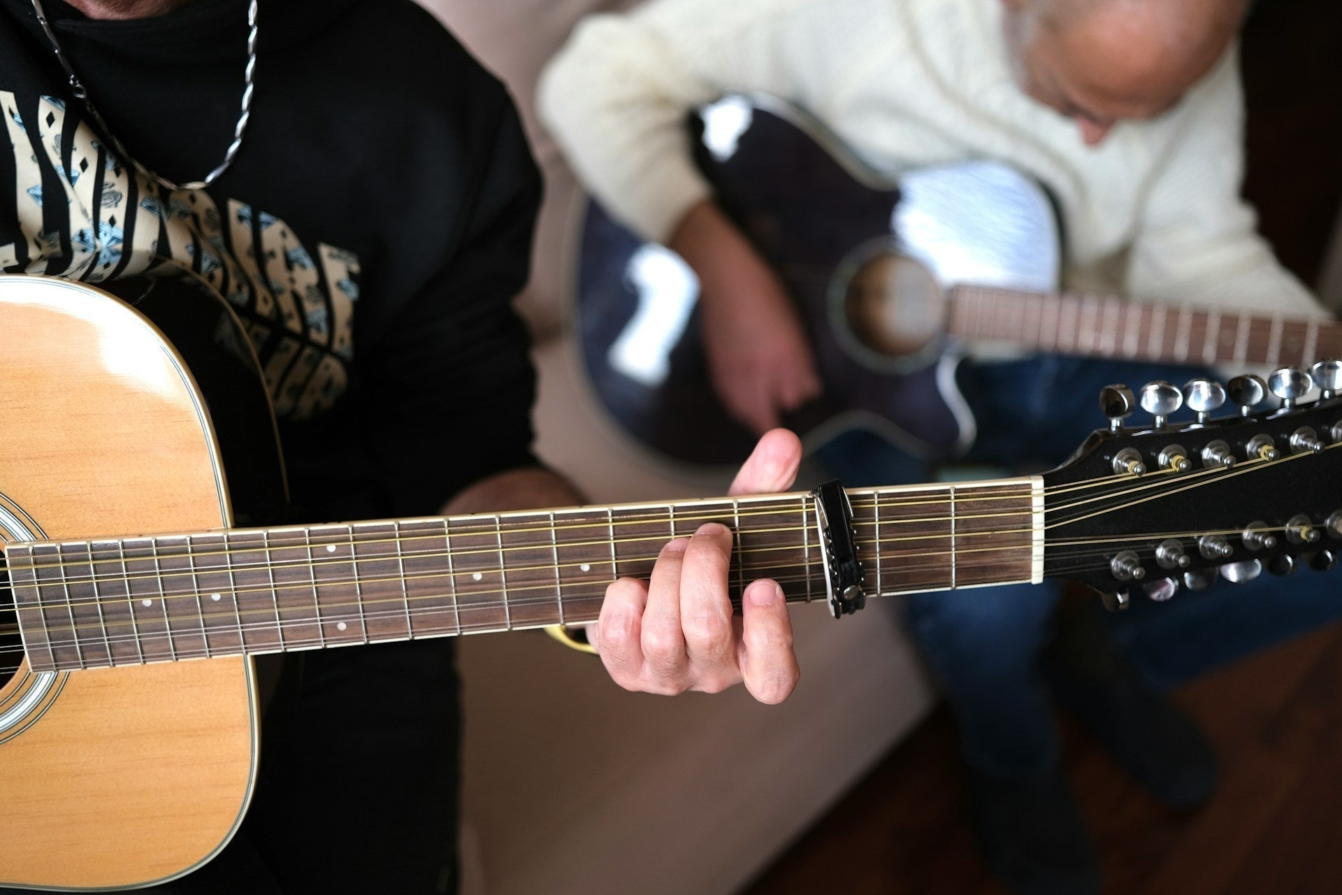two persons playing 12 string guitars with capo